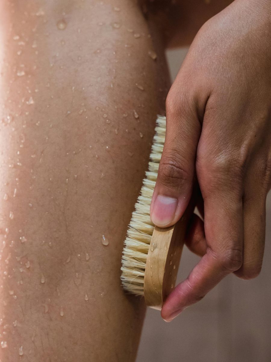 A wooden brush exfoliating skin beaded with water